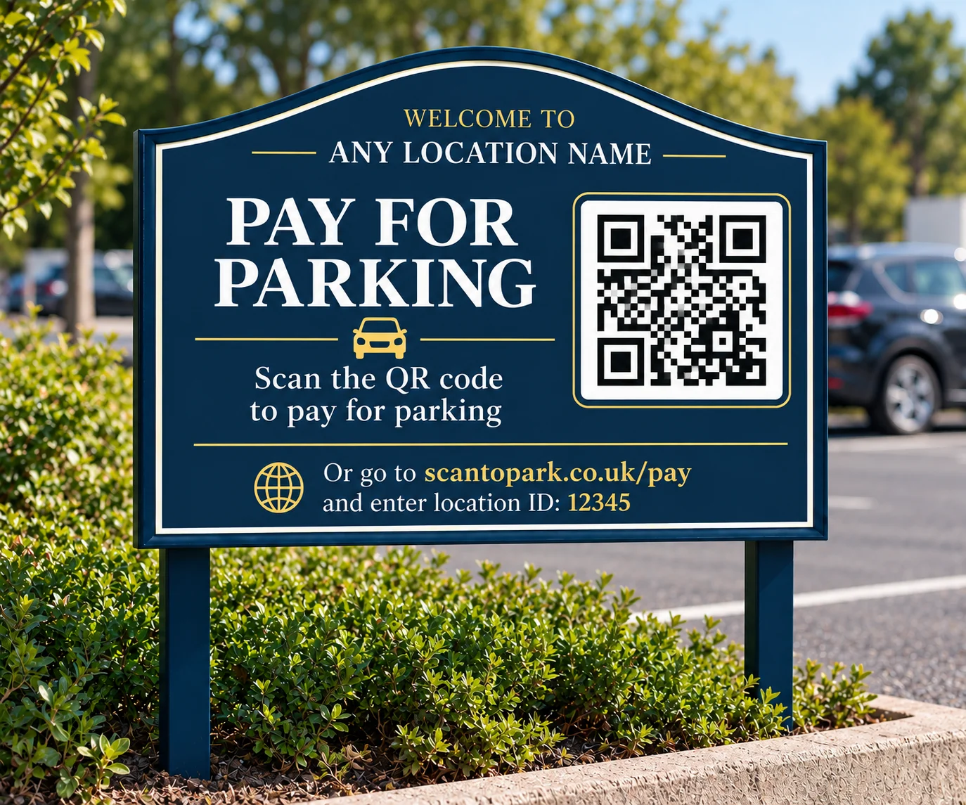 A navy blue entrance sign reading &ldquo;Pay for Parking — scan the QR code to pay for parking&rdquo;, with a QR code and a payment link to scantopark.co.uk/pay, standing in a planted bed beside the car park.
